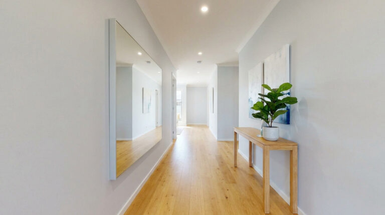 Un couloir lumineux avec un grand miroir mural, une console en bois et une plante verte.